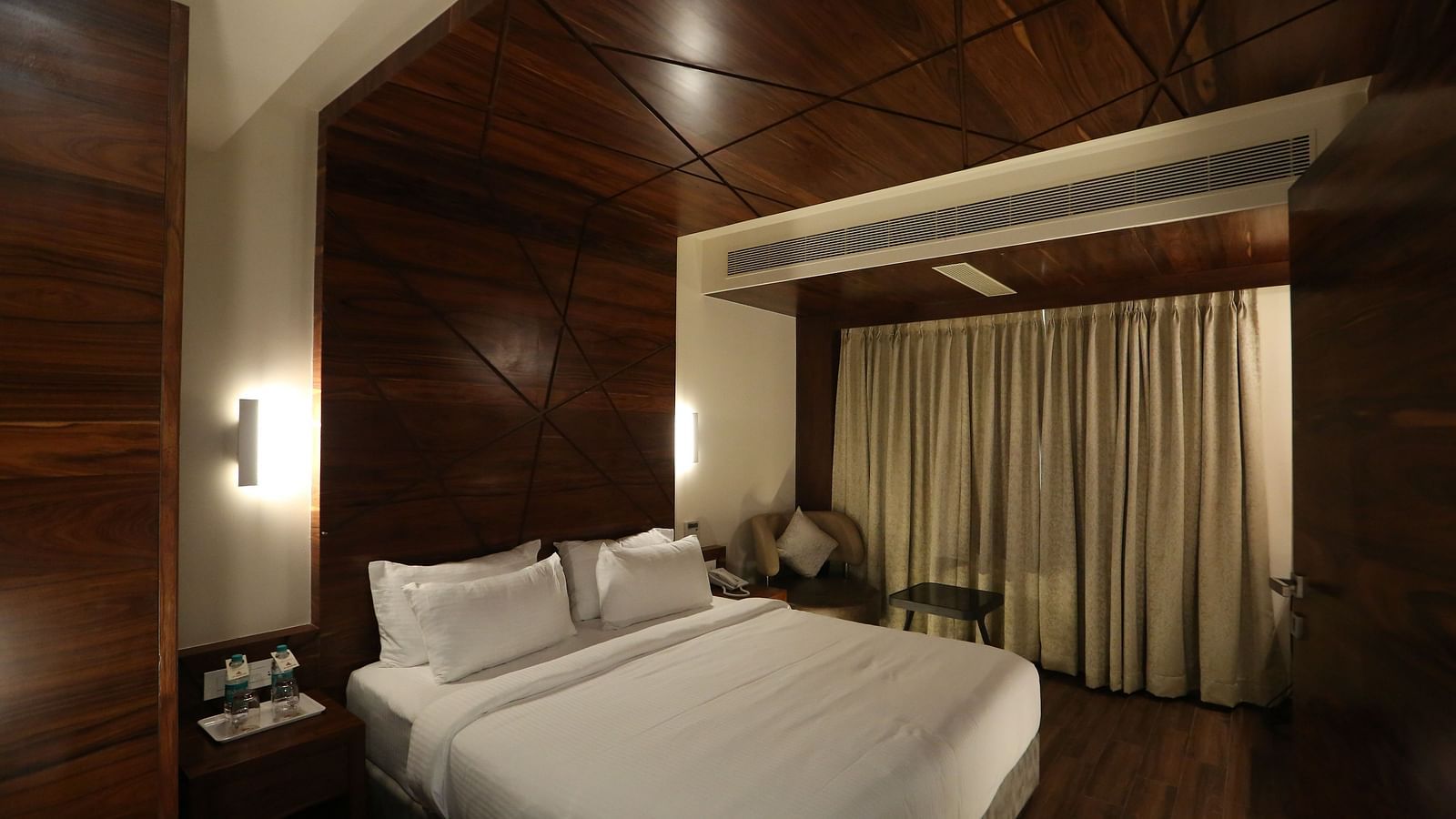 Premium Suite featuring a king size bed, bedside tables, lamps, and dark wood panelling - TGI SPS Grand, Coimbatore
