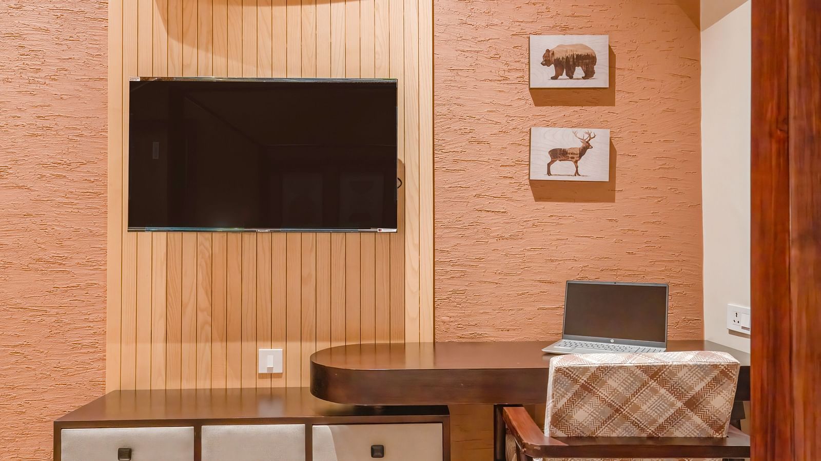 View of the desk, television right above it, and a table with a chair beside it, along with small wall-mounted frames at The Chamomile Estate.