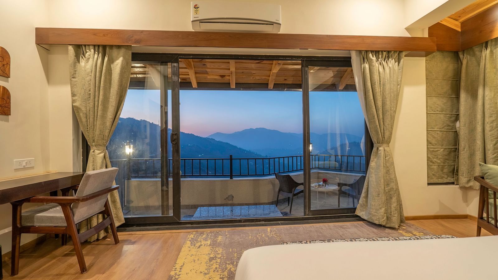 Spacious room with a bed, study desk, and chair beside the balcony overlooking a view at The Chamomile Estate.