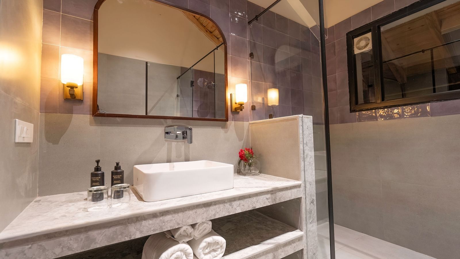 Well-lit bathroom with a sink and a large mirror, essentials placed beside the sink, and rolled towels stored below at The Chamomile Estate.