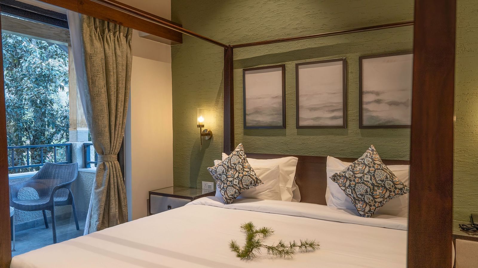 Four-poster bed with bedside tables and lamps, wall-mounted photographs above the headboard, and windows with curtains pulled to the side at The Chamomile Estate.