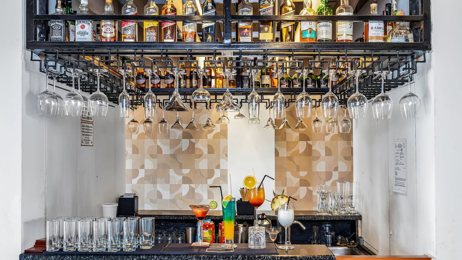 A well-stocked bar with various liquor bottles on shelves and wine glasses hanging upside down | The Citi Residenci Hotel Banskopa