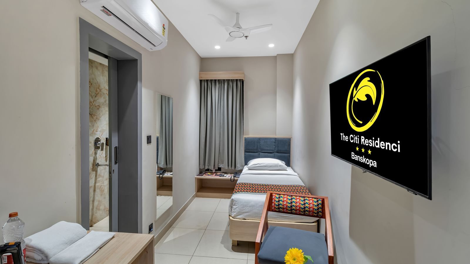 A compact hotel room with a single bed, a chair, a desk, and a wall-mounted television | The Citi Residenci Hotel Banskopa