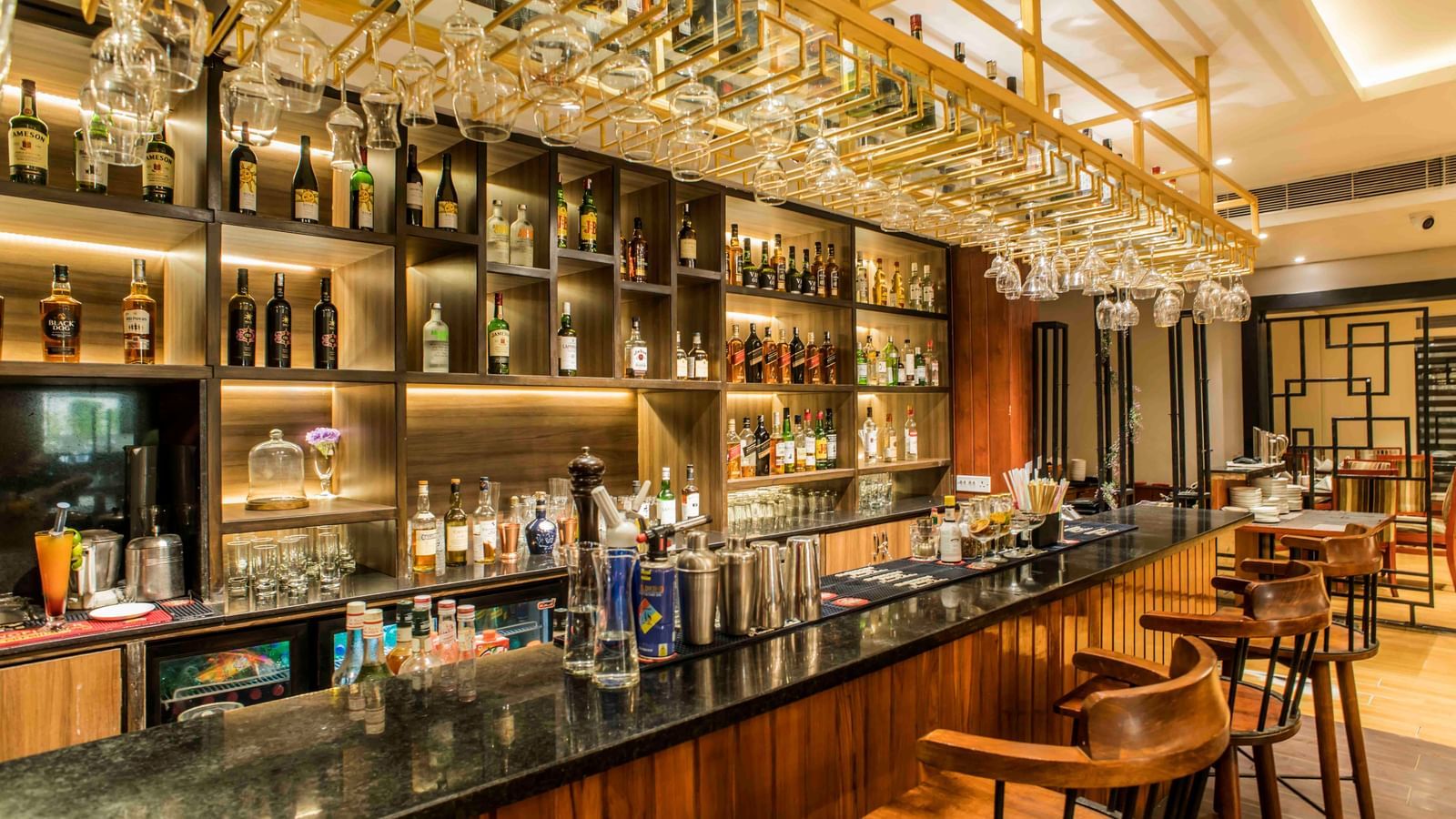 Well-stocked hotel bar with a dark countertop, multiple stools, and illuminated liquor bottles | The Citi Residenci Hotel Durgapur