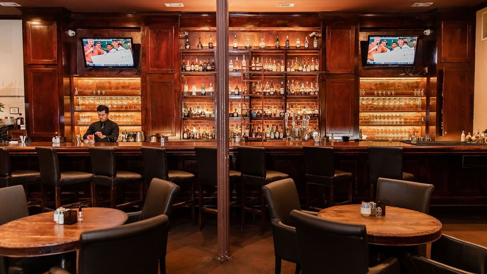 A bar area with round tables, a liquor display on the back wall, and mounted televisions above.- The Grand Hotel & Ballroom, McKinney