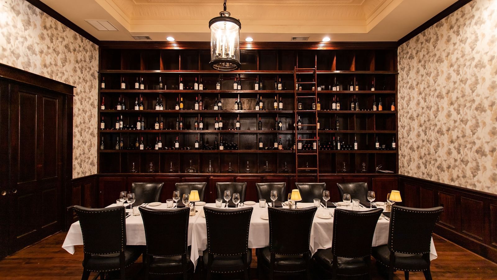 A  dining room with a long table, chairs, and a floor-to-ceiling rack of bottles against the back wall.- The Grand Hotel & Ballroom, McKinney