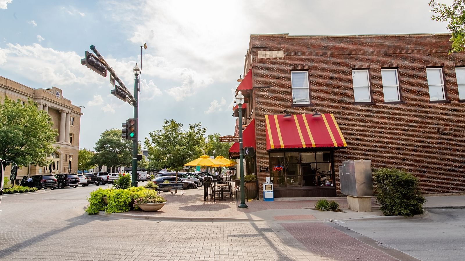 A commercial building with a striped awning, outdoor seating, and a wide pedestrian walkway in front.- The Grand Hotel & Ballroom, McKinney