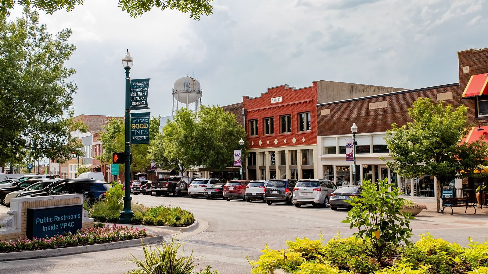 A town square with a welcome sign, a water tower in the background, and small businesses along the street.- The Grand Hotel & Ballroom, McKinney