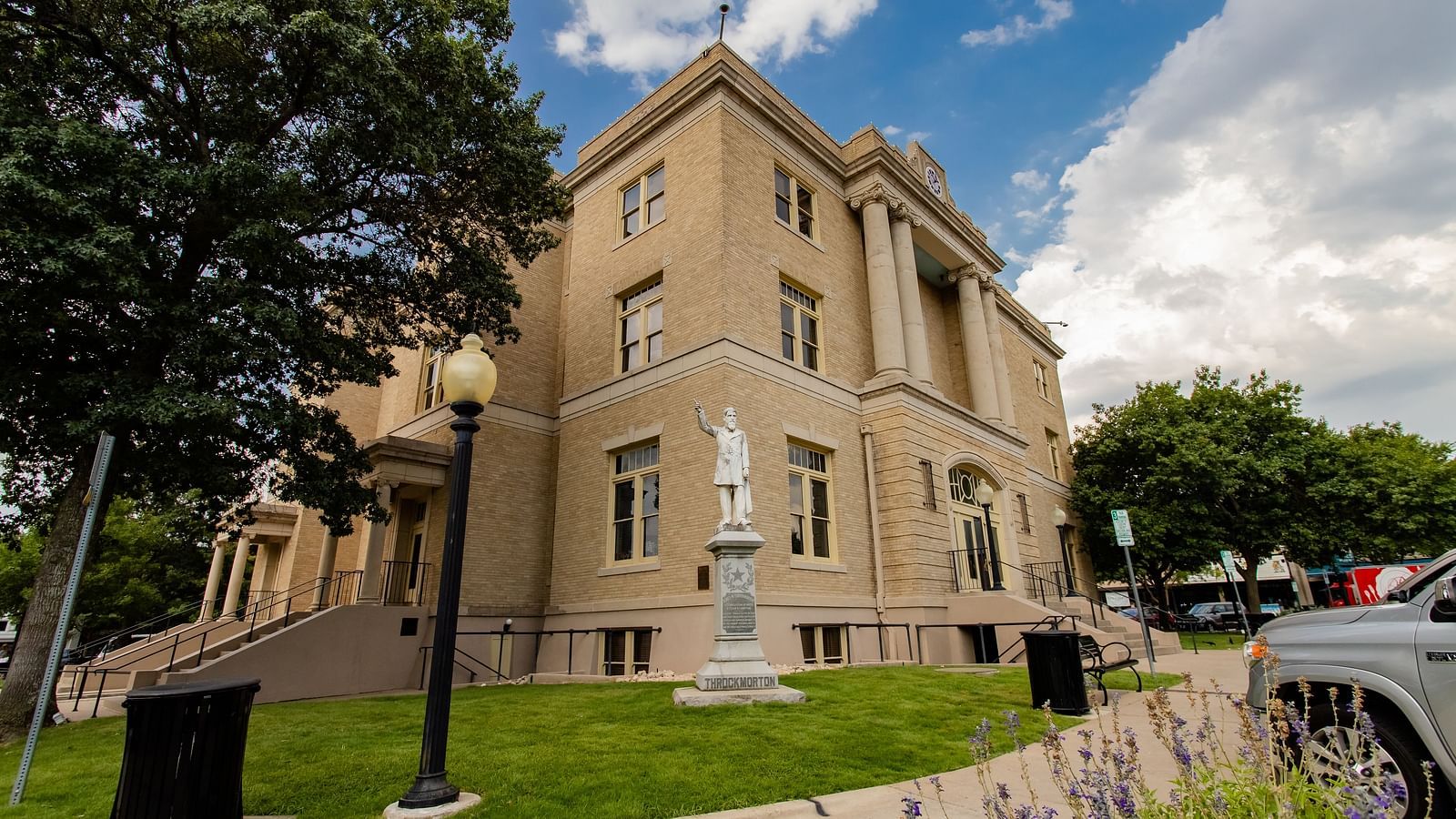 A historic courthouse with a grand entrance, surrounded by trees, shrubs, and a neatly trimmed lawn.- The Grand Hotel & Ballroom, McKinney