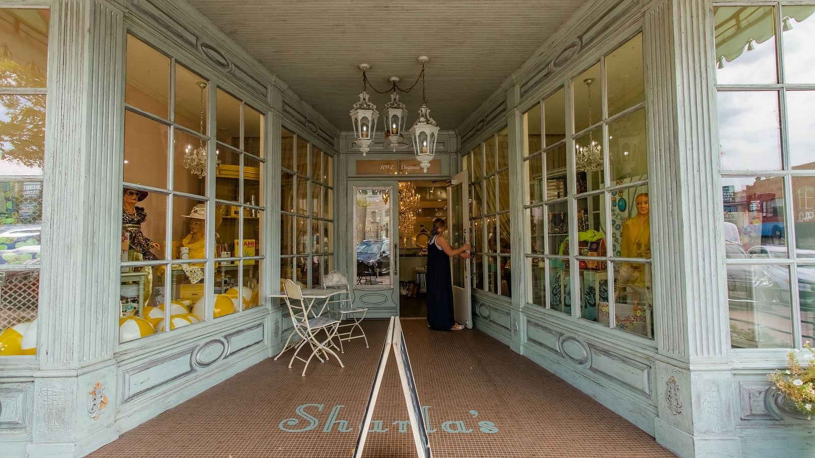 A boutique storefront with glass windows, a chandelier hanging in the entrance, and an elegant display inside.- The Grand Hotel & Ballroom, McKinney