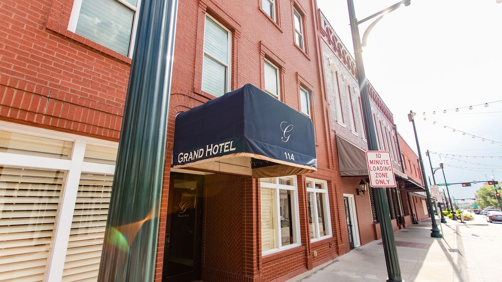 A  brick building with a row of windows and decorative trim, exuding a historic and timeless charm.- The Grand Hotel & Ballroom, McKinney