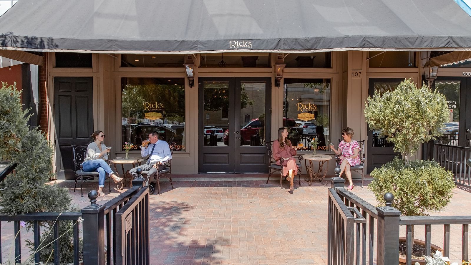 A restaurant entrance with a ramp and double doors, with people sitting near the outdoor seating area.- The Grand Hotel & Ballroom, McKinney