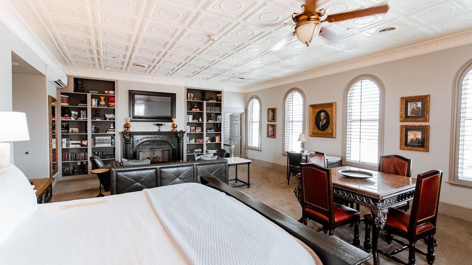 A large bedroom featuring a bookshelf with books, a cosy seating area, and a comfortable bed, providing a relaxing environment - The Grand Hotel & Ballroom, McKinney