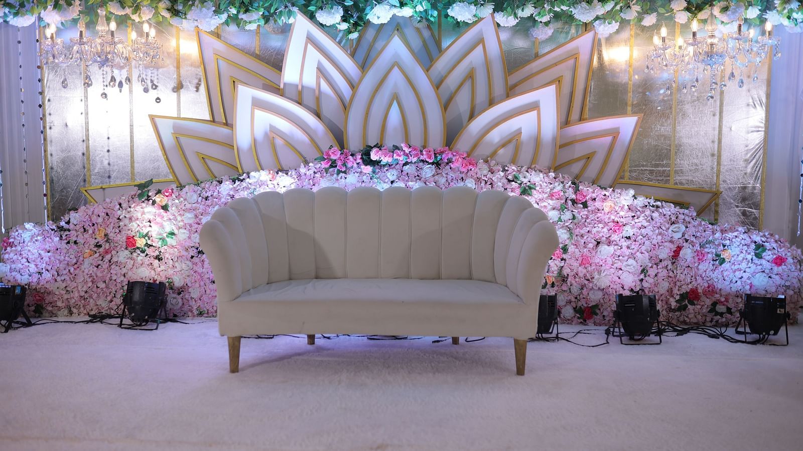 Empty love seat on carpet before a backdrop of lotus petals, and flowers, and soft lights, likely for a wedding reception - The Grand Legacy Resort and Spa
