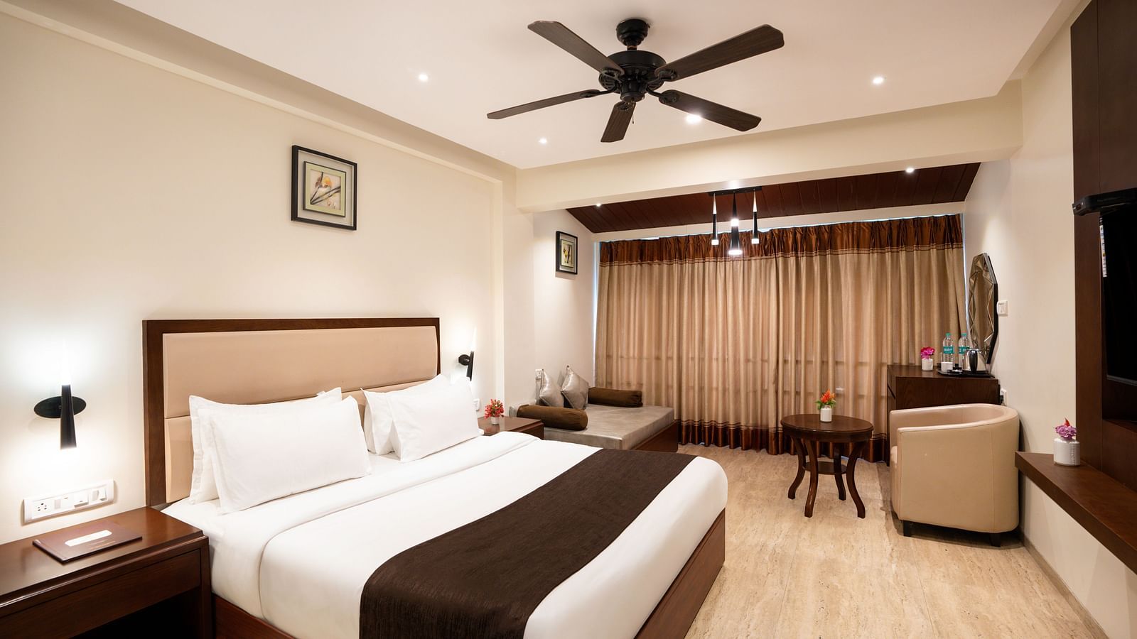 Spacious room with double bed, ceiling fan, and a sitting area with table - The Grand Legacy Resort & Spa