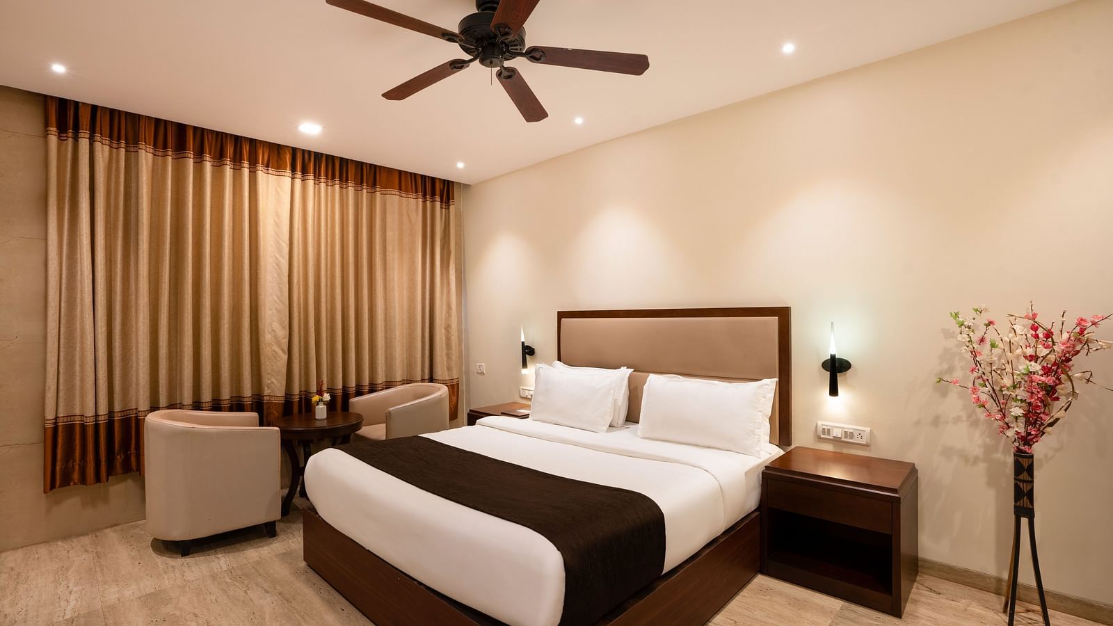 Shot of a spacious room with neutral toned walls featuring a king size bed, two small sofas, a centre table, flower vase and a side table | The Grand Legacy Resort and Spa