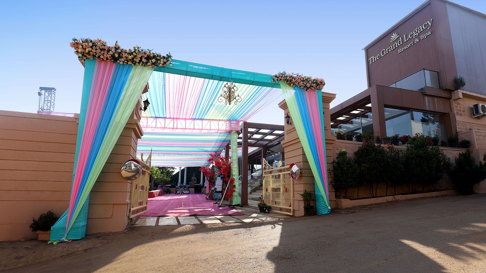 Entrance of a wedding area decorated with large and colourful fabric pieces, flowers, and other decorative elements at The Grand Legacy Resort & Spa