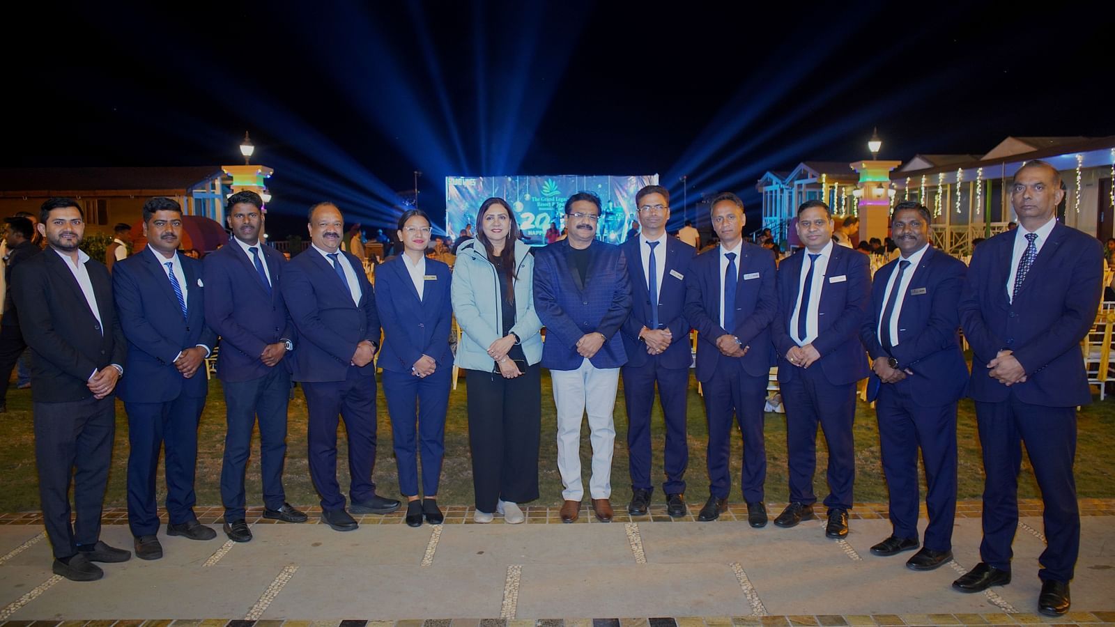 Formal group photo of staff members standing in a line at a night event - The Grand Legacy Resort & Spa