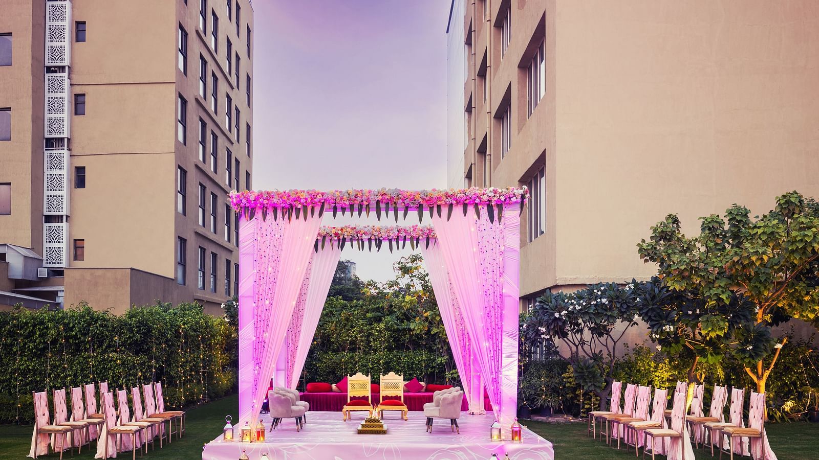 a stage set with two chairs and a canopy above and a group of chairs lined up on either side of the stage - The Hideaway Banquets & Lawns, Greater Noida