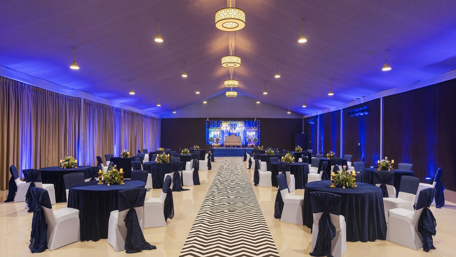 a pathway with clusters of tables and chairs on each side of the pathway and chandeliers lighting up the pathway throughout - The Hideaway Banquets & Lawns, Greater Noida