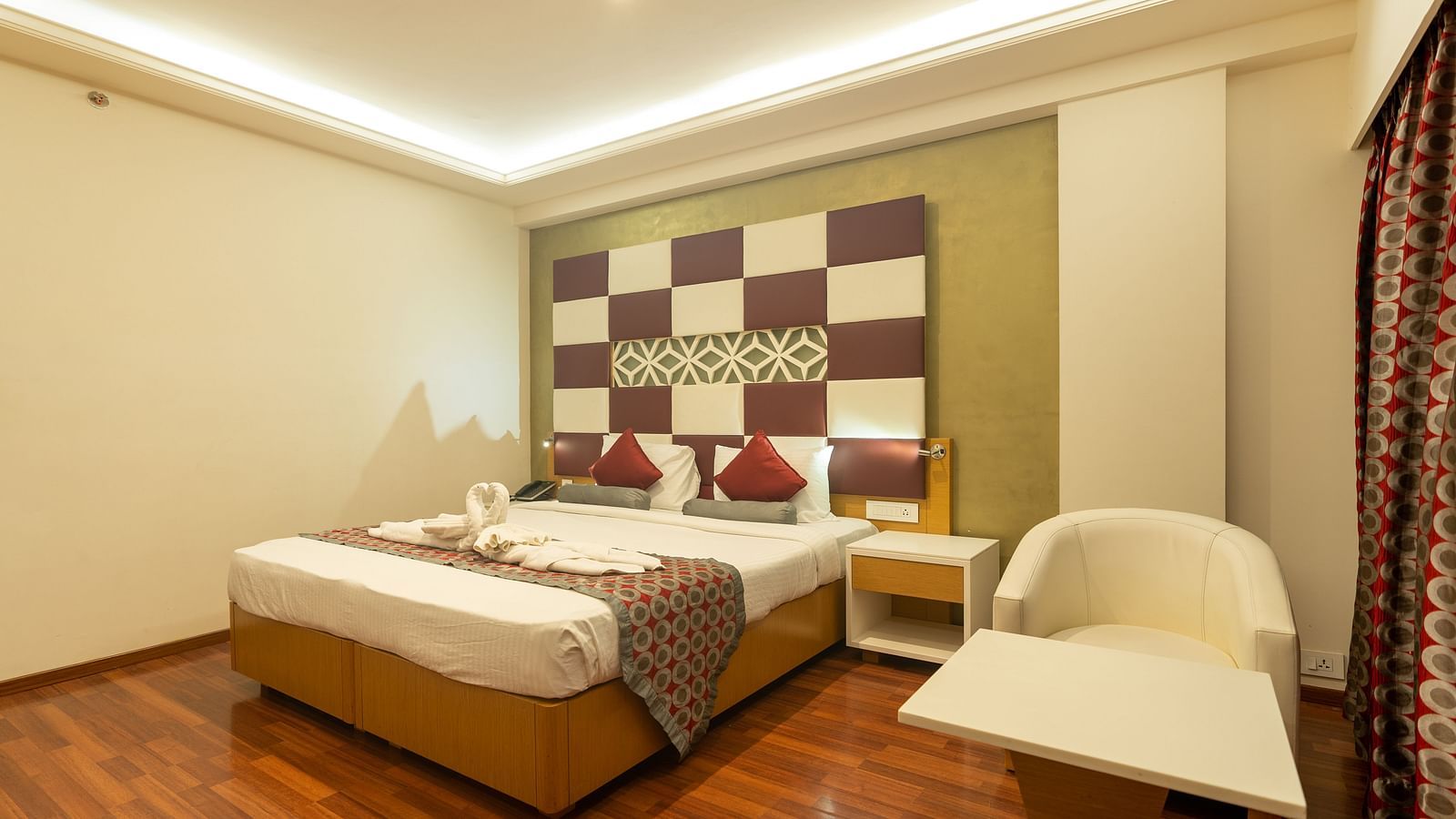king size bed with side table and a chair and table at The President Hotel, Hubli