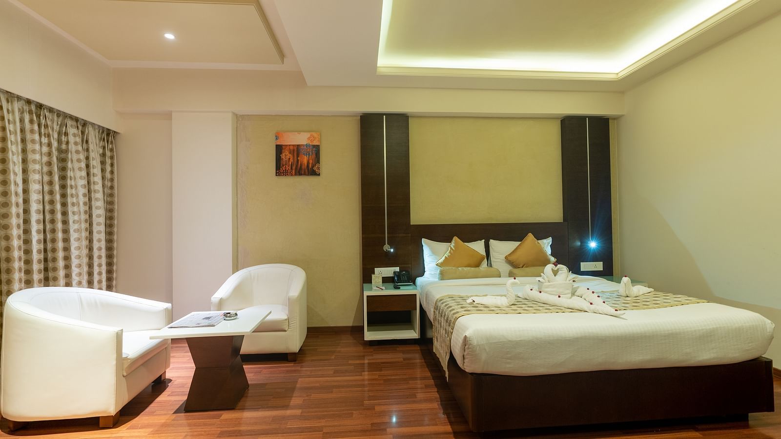 room with king size bed, a side table and a sofa set and table at The President Hotel, Hubli
