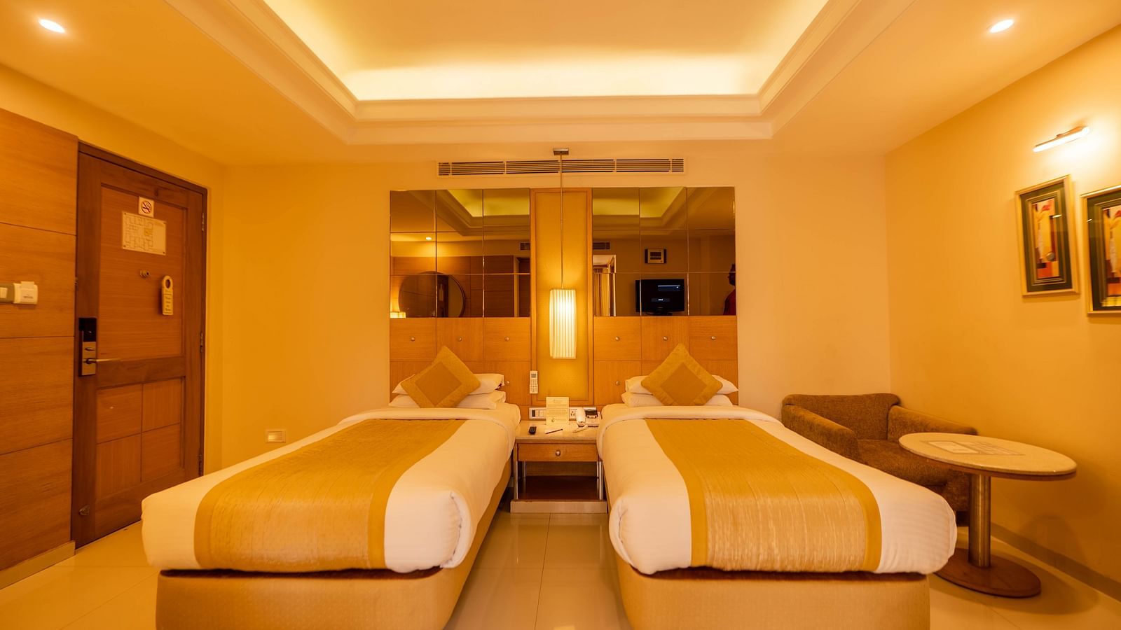 A warmly lit hotel room with twin beds and a soothing, neutral color palette- The President Hotel Jayanagar, Bangalore
