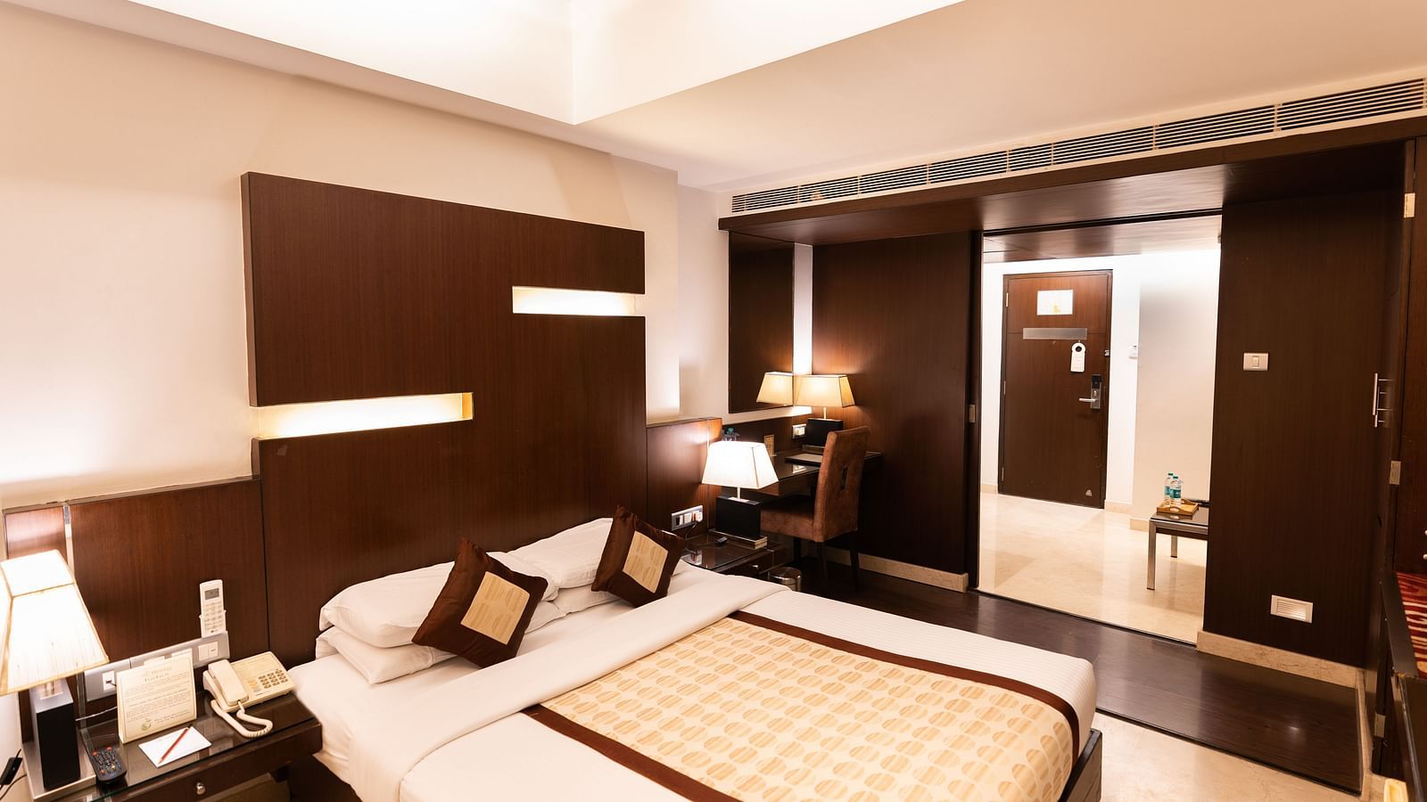 A modern hotel room featuring a large bed with brown headboard, sleek furnishings, and ambient lighting for a comfortable stay - The President Hotel Jayanagar, Bangalore