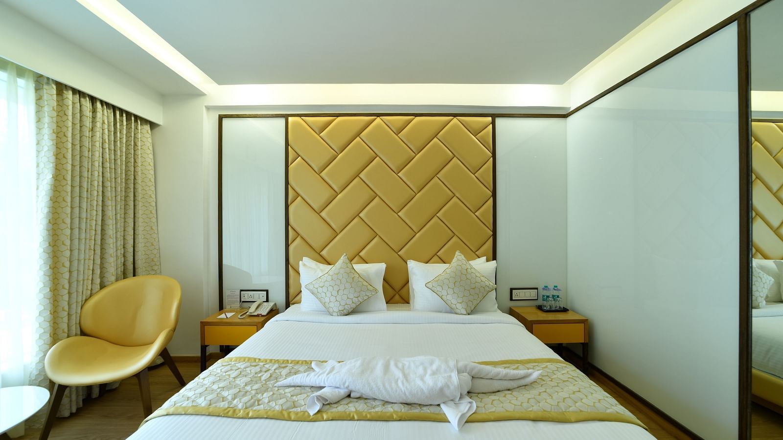 An image of a bedroom featuring a telephone and two water bottles neatly placed on either side of the bed - The President Hotel, Kumara Park, Bangalore