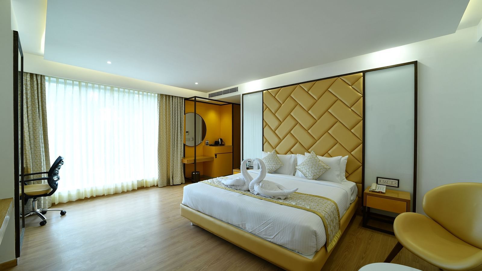 An image of a bedroom with a designed headboard and ample natural light passing through the window - The President Hotel, Kumara Park, Bangalore