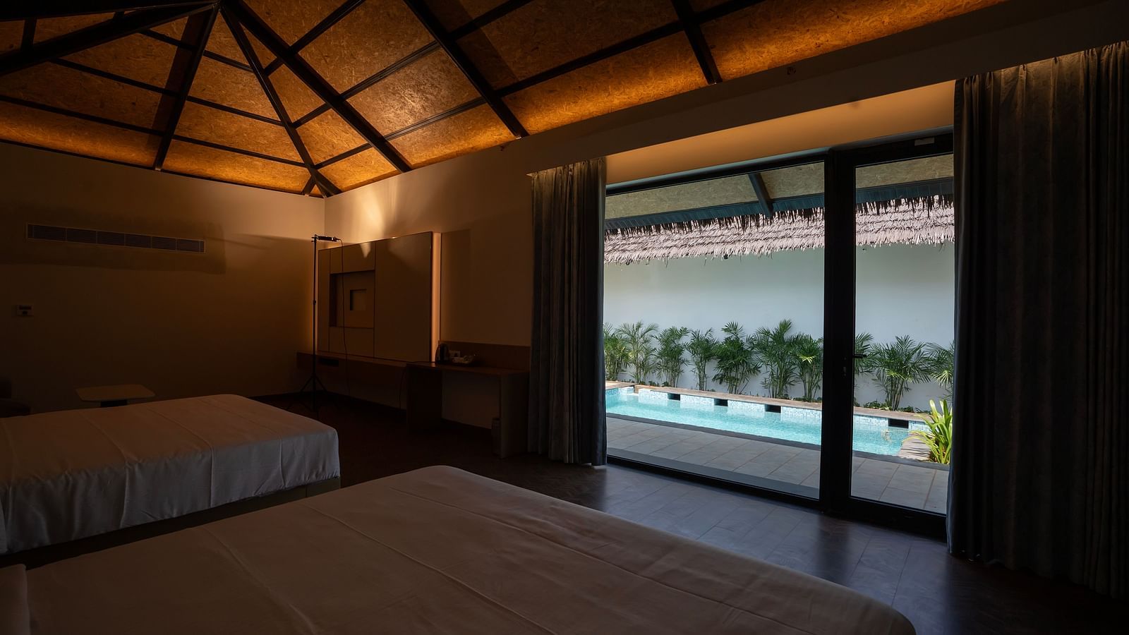 Dimly lit interiors of the bedroom of the Exotic Pool Villa overlooking the private swimming pool from the tall french windows at The Shore, Trishvam.