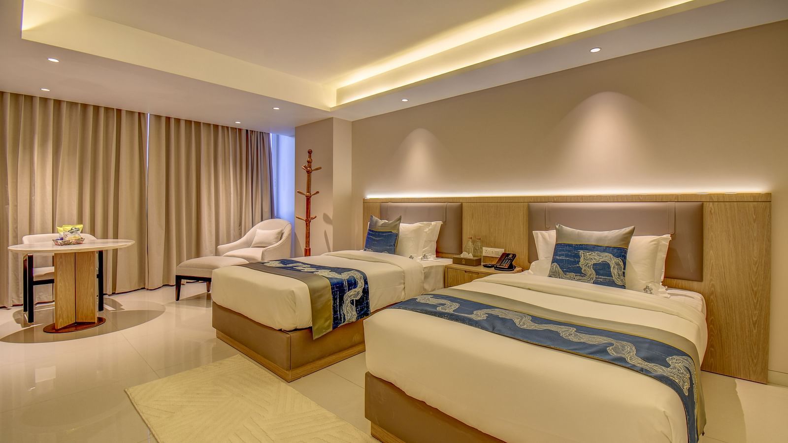 Side view of a well-lit Premium Twin room at The SSK Solitaire Boutique Hotel & Spa, Gangapur Road - Nashik featuring a twin  bed, two armchairs, a small table, and a work desk with a chair.