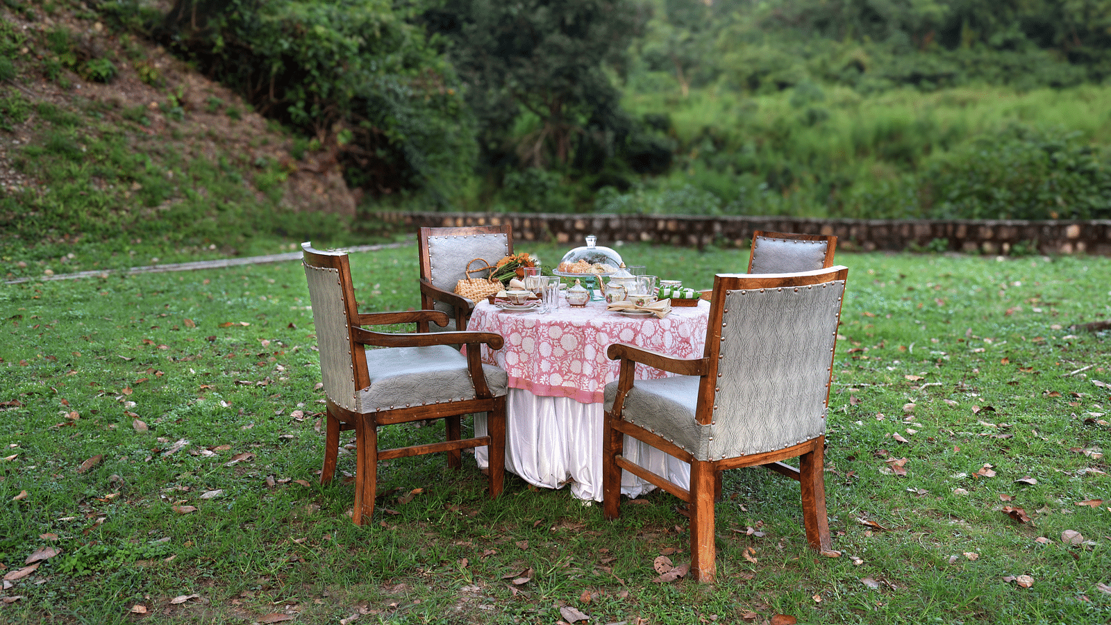 A view of the breakfast table surrounded by chairs placed in an open-air setting during the day at The Sylvan Retreat, Dehradun.