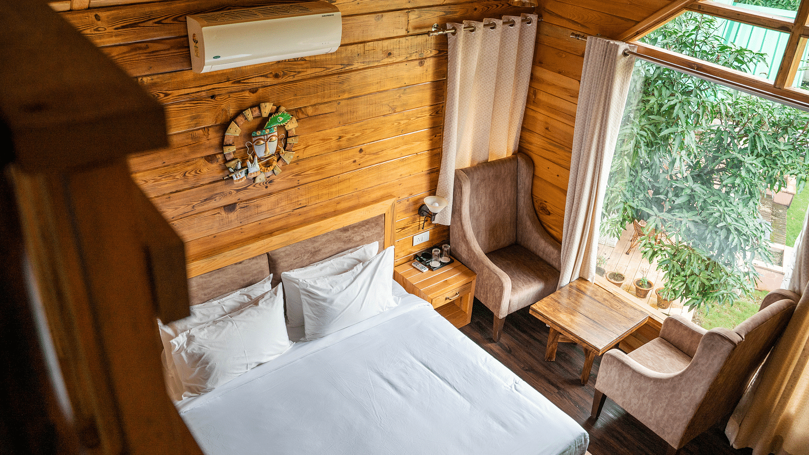 A view of the large bed alongside chairs placed near a large bed at Pinewood Cottage at the Sylvan Retreat, Dehradun.