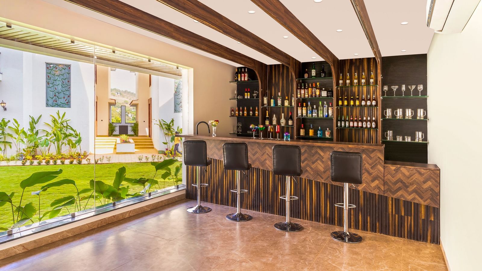 overview of the bar area with bat stools and a showcase with many bottles in it - The Tanisi Hotels & Resorts, Goa
