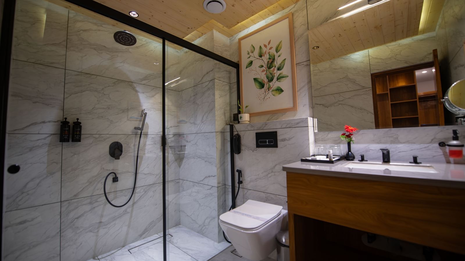 A bathroom in the Superior Room at the Tattva Devaprayag with a toilet, a wooden sink, and a shower with a glass door.
