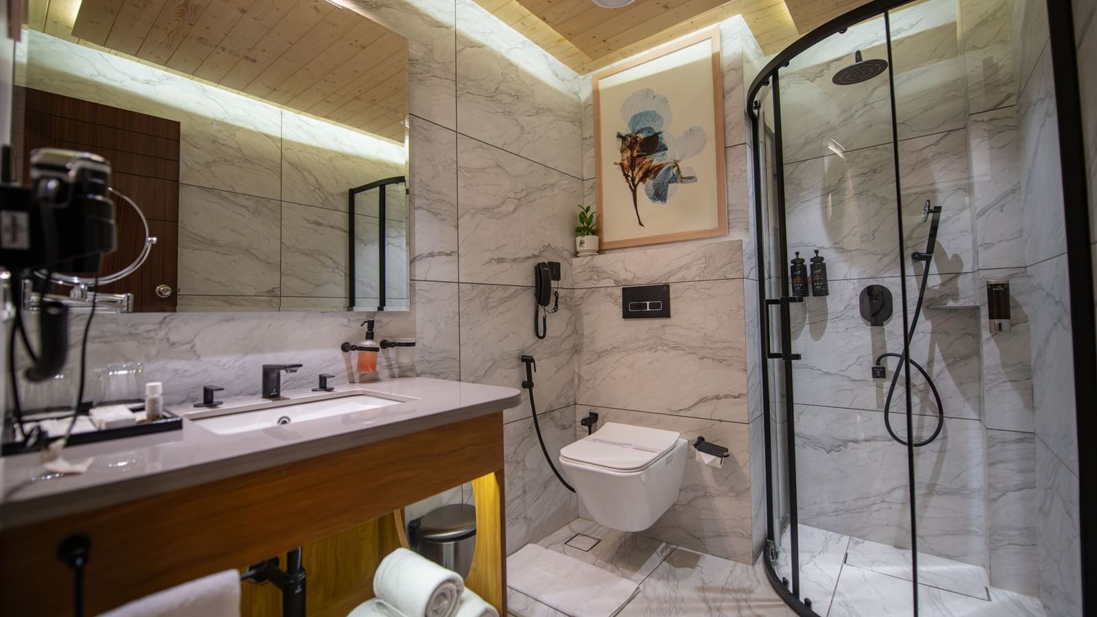 A washroom of the Executive Room at The Tattva Devaprayag with a toilet, a wooden sink, and a shower with a glass door.