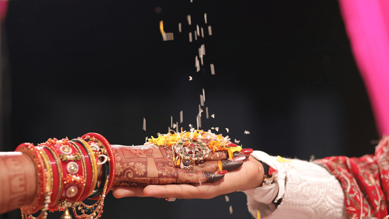 Bride has placed hand over the groom and coloured rice with the some petals are falling on their hands.