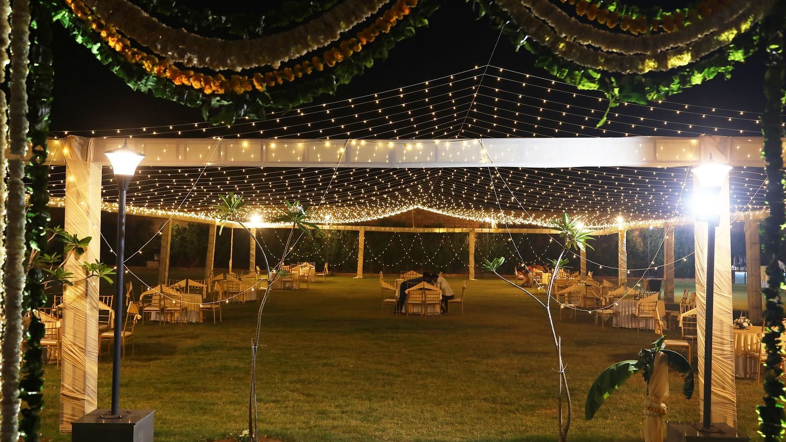 Lawn setup with chairs and lights under a canopy decorated with flowers at Tisya Farms, Gurgaon.
