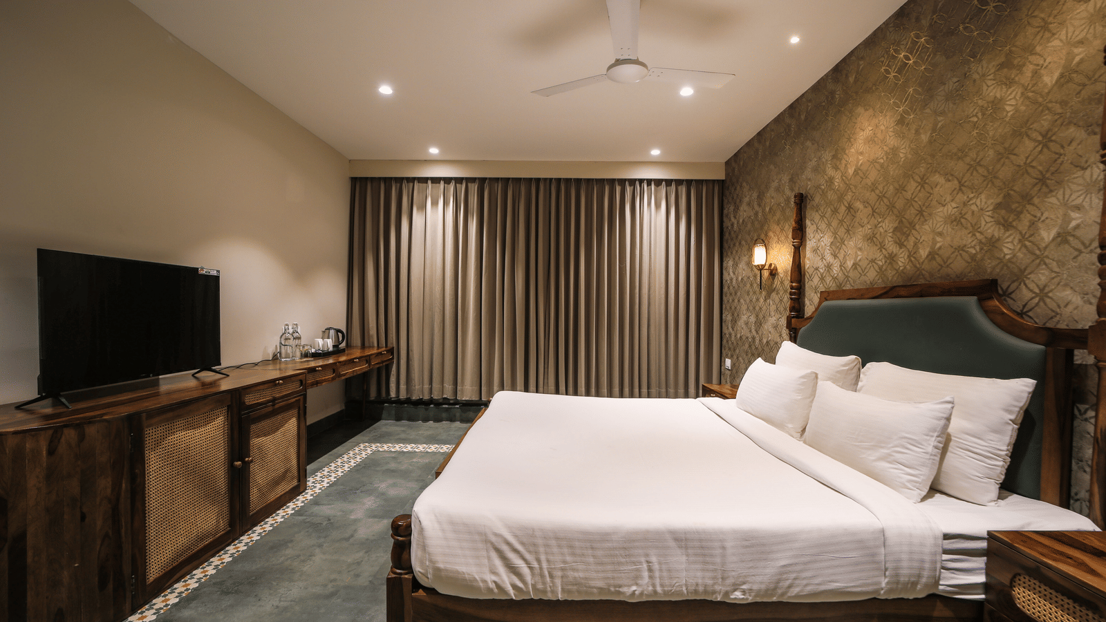 Bedroom featuring a king size bed against a patterned wall facing the TV in front of it under warm lighting at Trance Veechika Resort