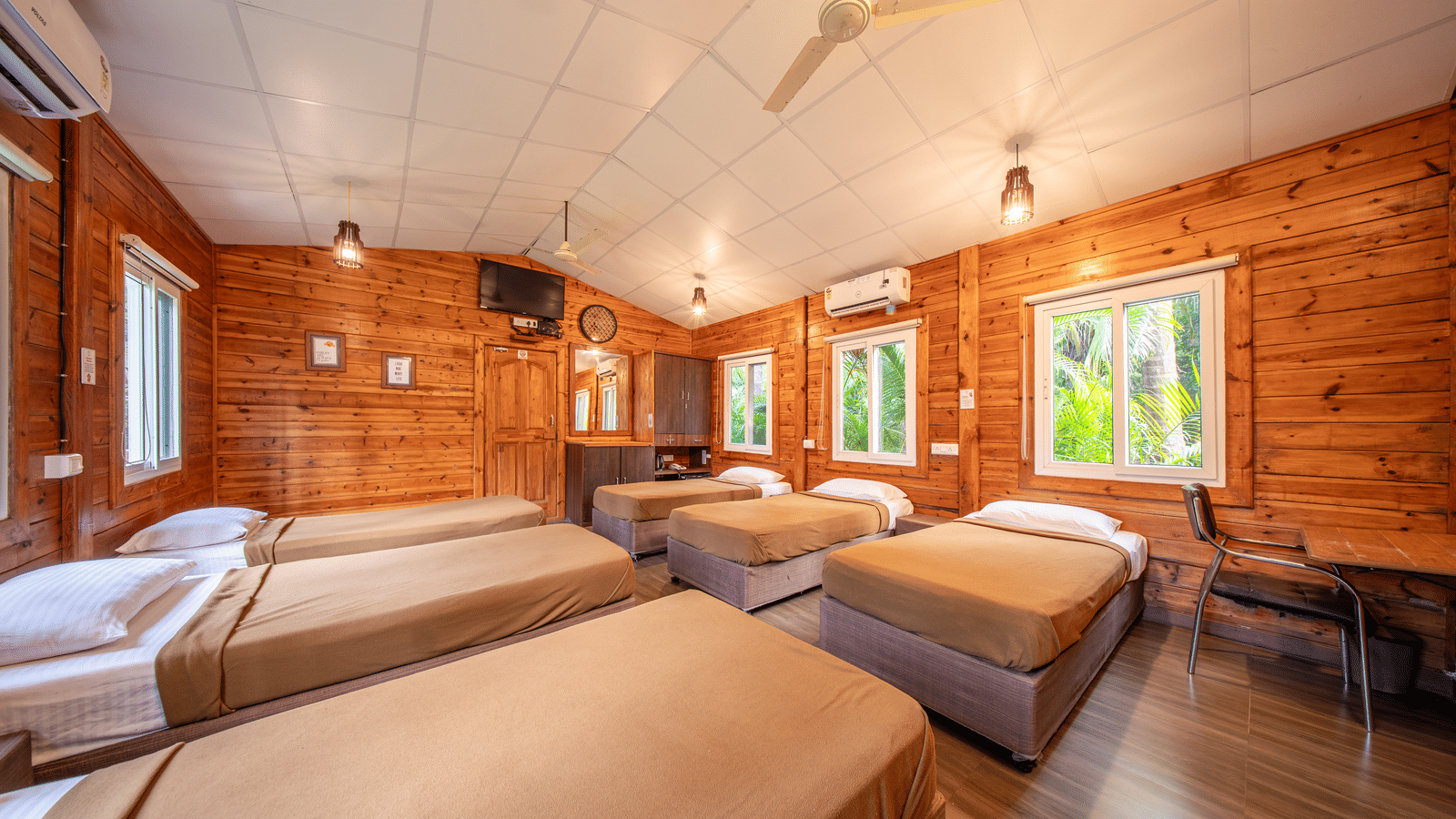 Family chalet with several single beds, wooden walls, large windows, ceiling fans, and chairs at Tranquil Beach Resort, Harihareshwar.