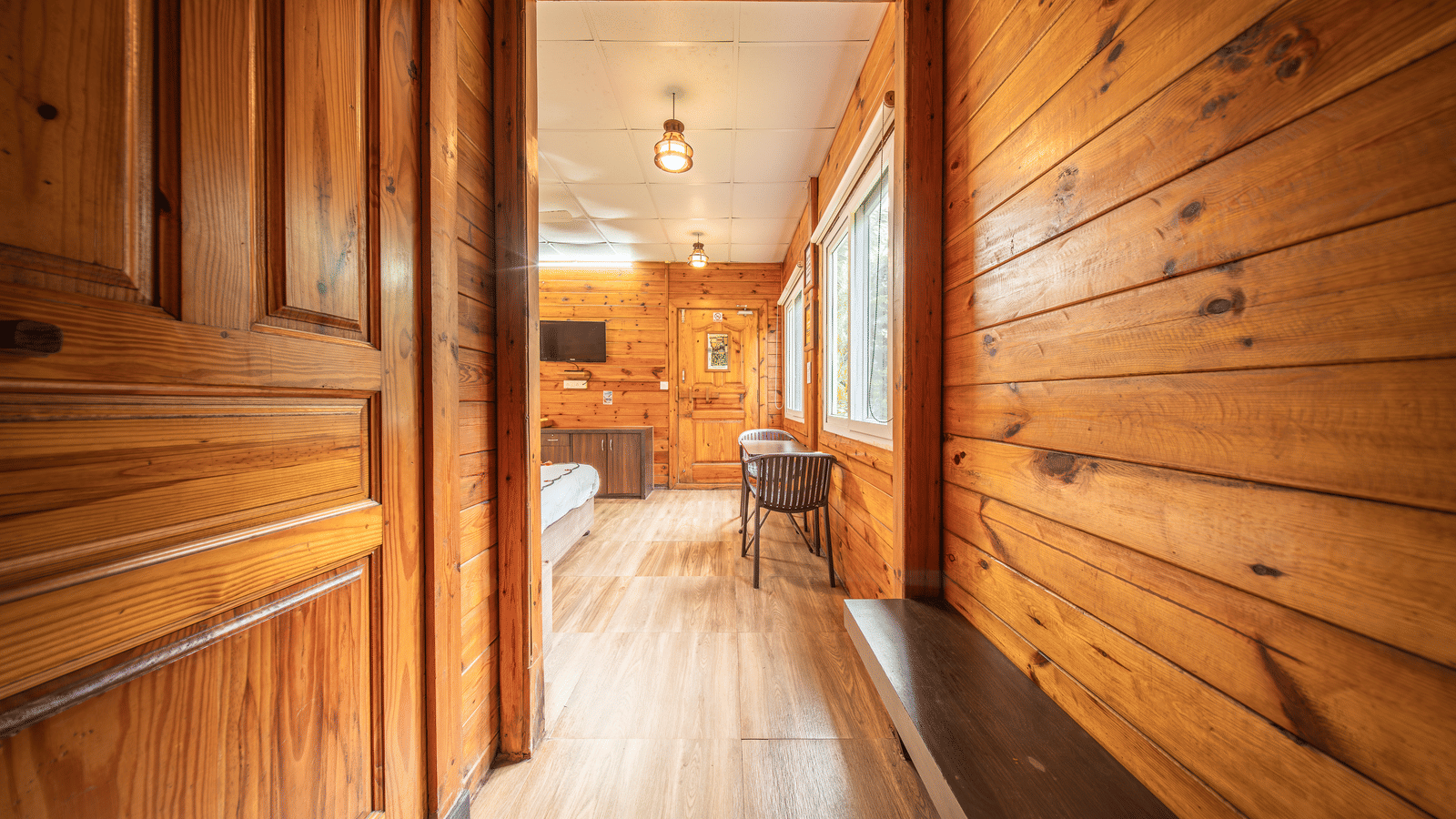 Hallway with wooden walls, windows, ceiling lights, and table, guestroom at Tranquil Beach Resort, Harihareshwar.
