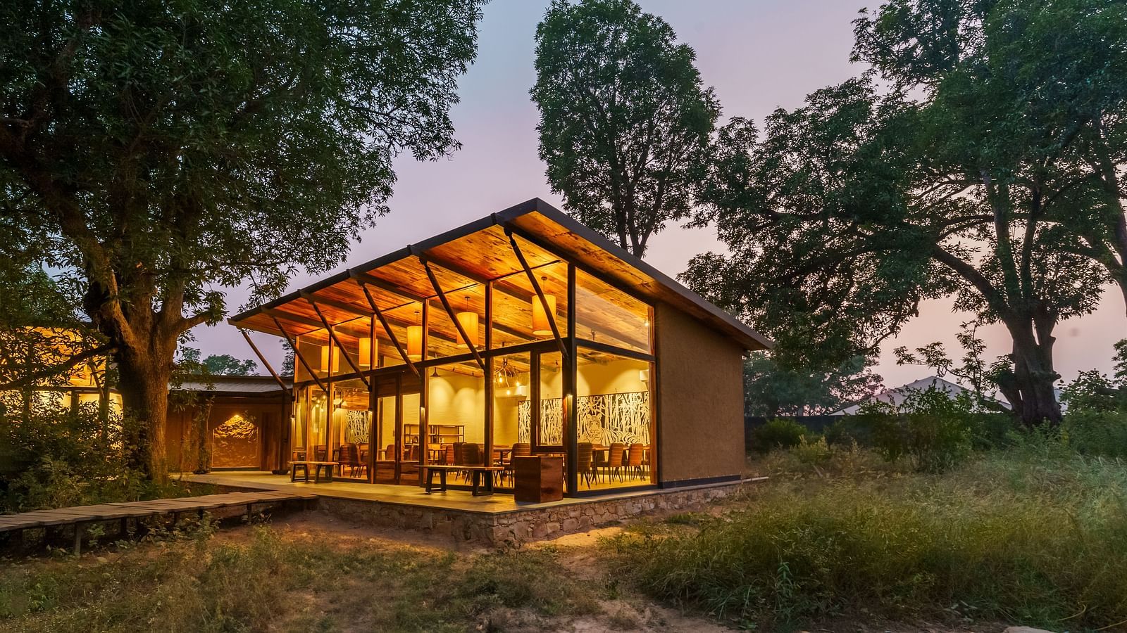 Facade view of a well lit cottage surrounded by trees at Trees N Tigers, Tadoba.