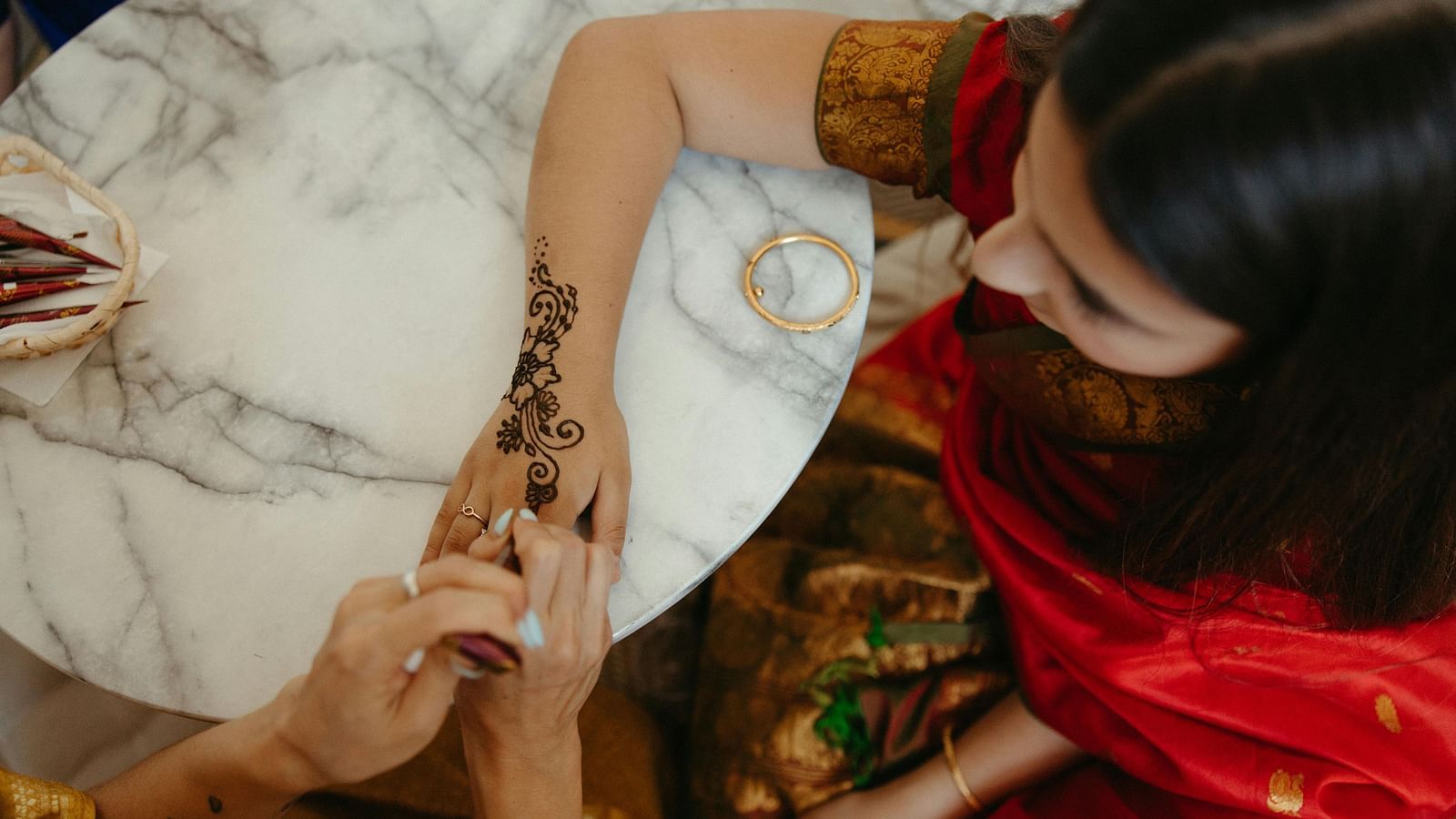 a woman dressed in a red saree getting her hand designed with henna