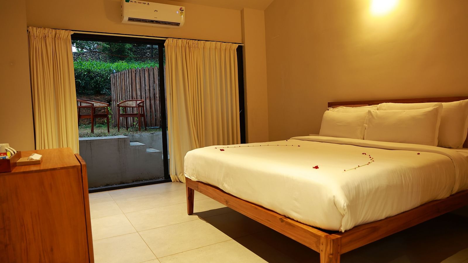  A hotel room at Vaasta Vagamon featuring a bed with subtle petal decor, a wooden cabinet, and a sliding door leading to an outdoor patio.