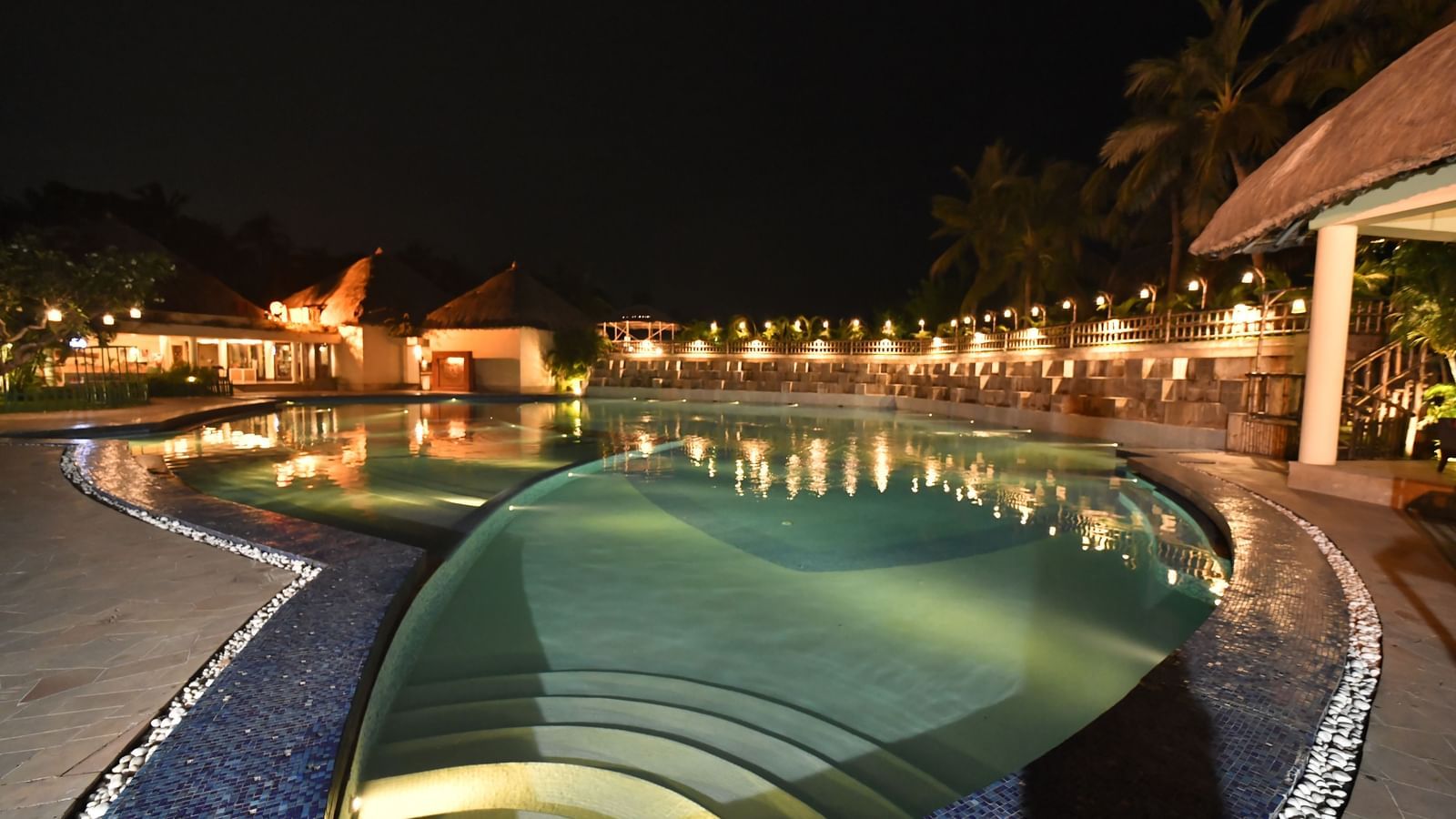 A swimming pool area is illuminated at night, surrounded by resort-style architecture
