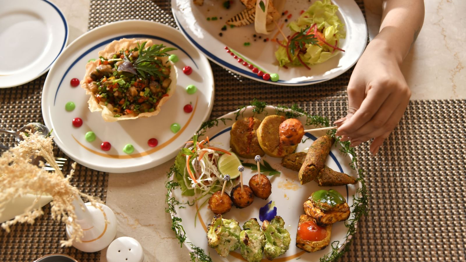 Hands are seen reaching for food served on plates, indicating a meal | Yagna