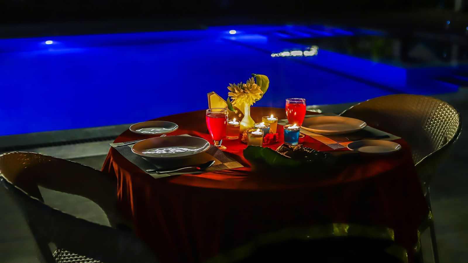 A poolside dining arrangement with a decorated table and chairs is illuminated at night at Vedikant Resorts The Mallard Corbett.