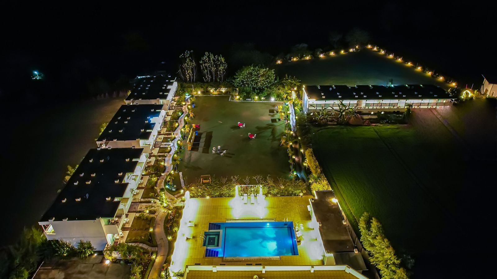 Night view of a swimming pool and buildings decorated with lights from top angle - Vedikant Resorts The Mallard Corbett.