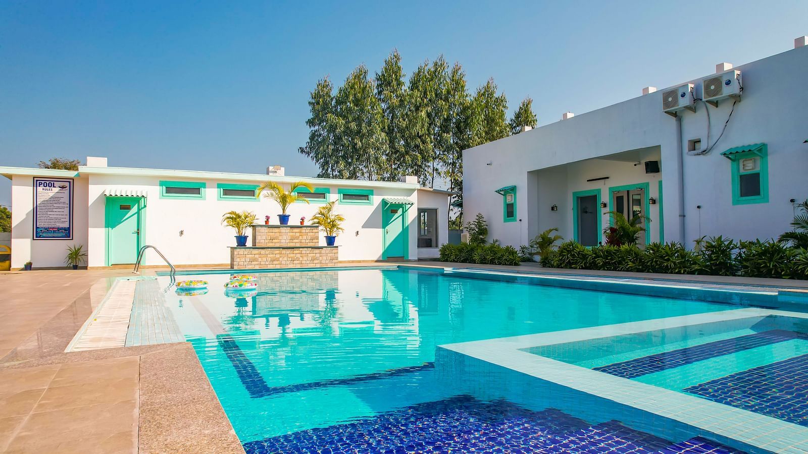 View of a swimming pool with buildings, trees and clear blue sky in the background - Vedikant Resorts The Mallard Corbett.
